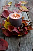 Candle in wreath of autumnal cherry leaves on rustic wooden surface