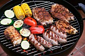 Marinated pork steaks, sausages and vegetables on a barbecue