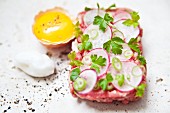 Steak tartare topped with radishes and parsley garnish with an egg and truffle foam next to it