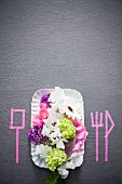 Place setting with summer flowers and silhouettes of cutlery marked on grey surface with pink washi tape