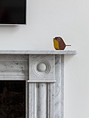 Kleiner minimalistischer Holzvogel auf Marmor-Kaminverkleidung platziert
