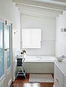 Weisses Bad, holzverkleidete Badewanne und halbhohe Holzbrüstung an Wand in elegantem Landhausstil