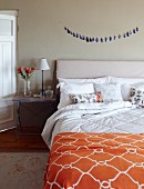 Doppelbett mit Kopfteil, im Vordergrund orangefarbenes Plaid mit Rautenmuster, seitlich rustikaler Nachttisch, in ländlichem Schlafzimmer