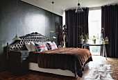 Double bed with antique headboard, Union Flag scatter cushions and fur blanket in bedroom with dark-painted walls and dark grey curtains