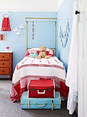 Stacked pale blue and red vintage suitcases at foot of child's bed with canopy frame in girl's bedroom painted pale blue