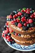 A layered chocolate cream cake decorated with berries and mint leaves