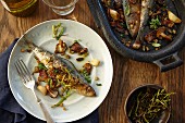 Roasted sardines with vegetables and herbs in an iron pan and on a plate