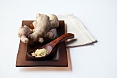 Grated ginger on a wooden spoon in front of a ginger root