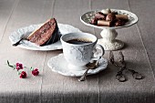 A cup of coffee with a slice of cake and various pralines