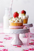 Strawberry yogurt cupcakes decorated with pink bows on cake stands and a bottle of milk with a straw in the background