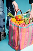 A woman holding a shopping bag of fresh fruit and vegetables