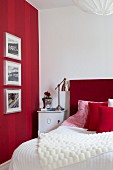 Framed pictures on red striped wall, bed with red headboard and retro-style lamp on bedside table