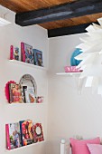 Books on narrow wall brackets and artichoke designer lampshade in foreground