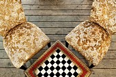 Tisch mit eingebautem Schachbrett und antike Stühle mit Goldmuster auf rustikalem Holzdielenboden