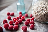 Fresh raspberries and a jar of oats on wooden table