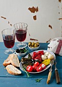 An appetiser platter with stuffed vine leaves and vegetables, white bread and red wine