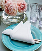 A vase of roses and a place setting with cutlery wrapped in a napkin on a table