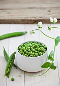 A bowl of fresh peas with pods and flowers