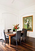 Chairs with grey upholstery around flower arrangement on elegant dining table; large, framed retro poster on wall within stucco panel