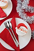 A Father Christmas cupcake on a plate with a napkin and cutlery