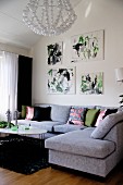 Modern, pale grey corner sofa in living room below drawings on wall