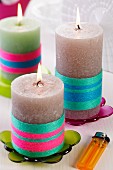 Kerzen mit farbigem Wollgarn umwickelt, auf bunten, transparenten Untersetzern