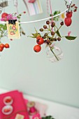 Sprigs of rose hips in tiny glass bottles hanging from white metal wreath