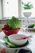 Place setting with white bowl in front of red bowl of vegetables on table