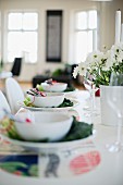 Place settings decorated with white bowls and savoy cabbage leaves and vase of flowers on table