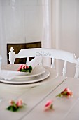 Roses and place setting on white wooden table and chair with name on backrest