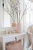 Vase of twigs and ornamental letters on white console table below framed mirror