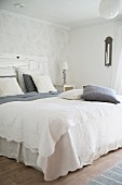 Double bed with white bedspread and grey and white pillows and scatter cushions in simple bedroom