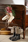 Wollsocken mit Orchideenblüten und Zimtstangen als Weihnachtsdekoration an Holzbettgestell, davor Vintage Stiefel
