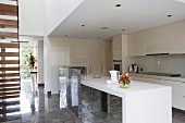 Open-plan, designer fitted kitchen with white counter and glossy stone floor in modern house