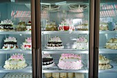 Various different celebratory cakes in a refrigerated display cabinet