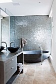 Designerbad mit runder Wanne vor grau schimmernder Wandstruktur und Waschtisch mit anthrazitfarbener Schüssel
