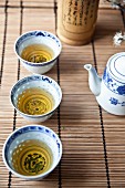 Drei asiatische Teeschälchen mit Grüntee auf Bambusmatte