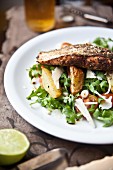 Grilled Cajun salmon steak on a bed of potato wedges and rocket and tomato salad with Parmesan