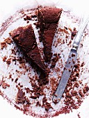 Two slices of chocolate cake on a plate with cake crumbs and a knife