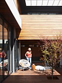 Young woman on sunny terrace with shell chair and stool