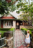 Little girl walking through garden gate and tiled path leading to country house with veranda