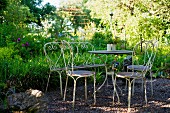 Idyllic, vintage seating area with metal bistro table and chairs on gravel floor in garden
