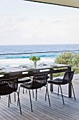 Black mesh chairs around set table on wooden deck with panoramic view of Pacific Ocean