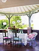 Tablecloth on table and white wooden chairs on dark wooden terrace with white, circular wooden roof