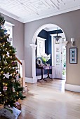 Christmas tree in hall with large, arched open doorway and view into vestibule of traditional house