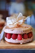 A macaroon cake with raspberries tied with a ribbon