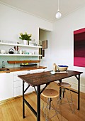 Vintage, industrial-style table and stool in front of white kitchen counter and narrow crockery shelves