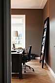 Desk and magazine rack leaning against wall in home office space with grey-painted walls