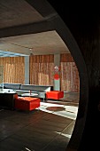 Blick durch kreisförmige Öffnung in minimalistischem Lounge-Bereich mit Sofagarnitur in Grau und Orange, im Hintergrund Bambusstäbe in Fensternischen als Sichtschutz