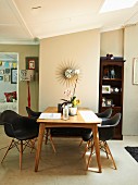 Dining area with black designer chairs around wooden table; sunburst clock on wall